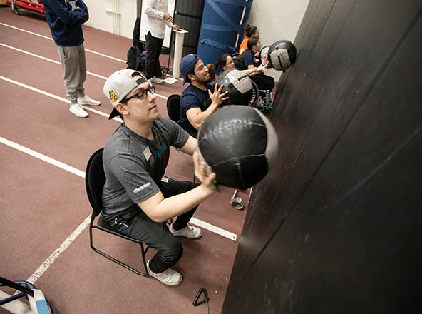 Male in chair throwing a ball against a wall for exercise